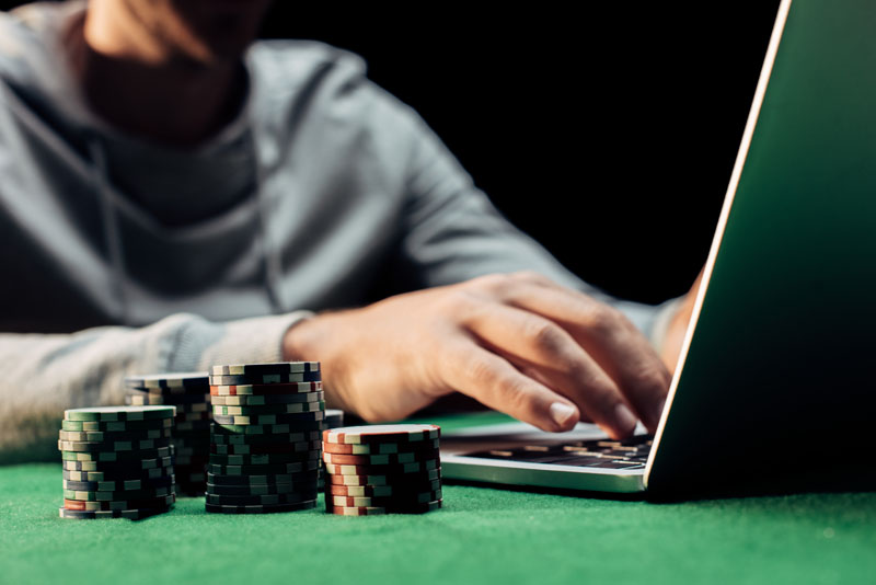 cropped view of man typing on laptop near poker chips isolated on black